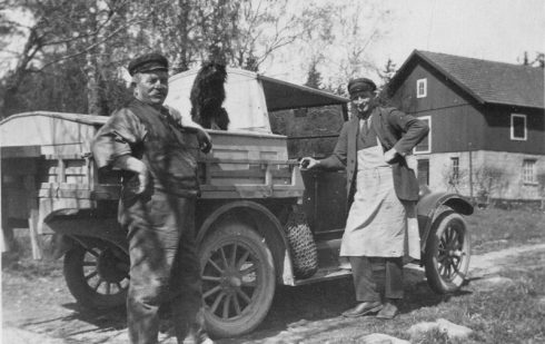 John Aronsson (till höger), kommer med kött till skomakare Albert Eriksson (till vänster). Hunden sitter på köttlådan och vid fotsteget hänger löksäcken. Foto är taget 1930 av Linnéa Eriksson, dotter till Albert Eriksson på bilden.